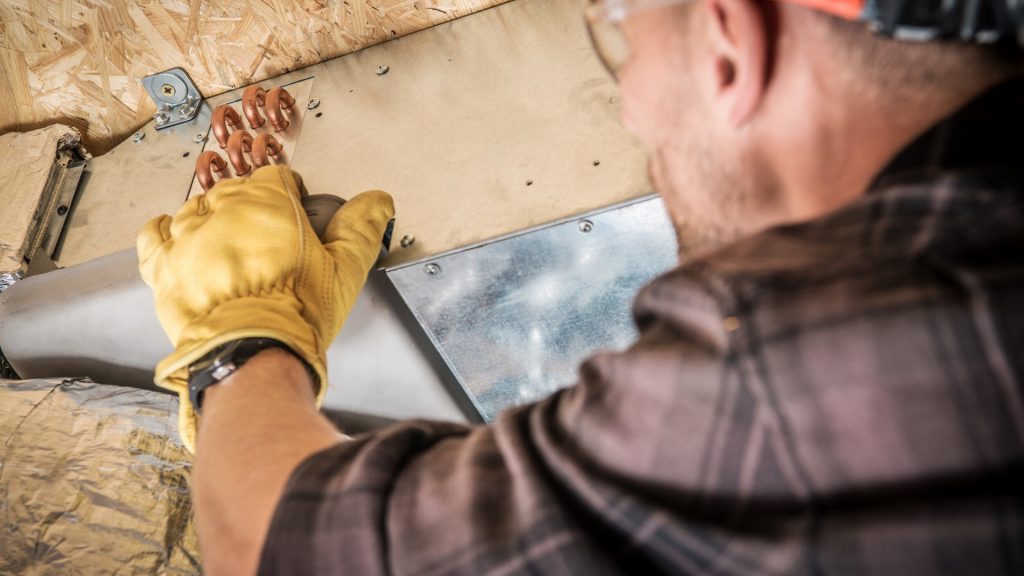 Man in flannel shirt with yellow gloves working on an air duct