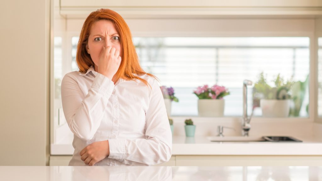Woman plugs her nose and makes disgusted face in a white kitchen