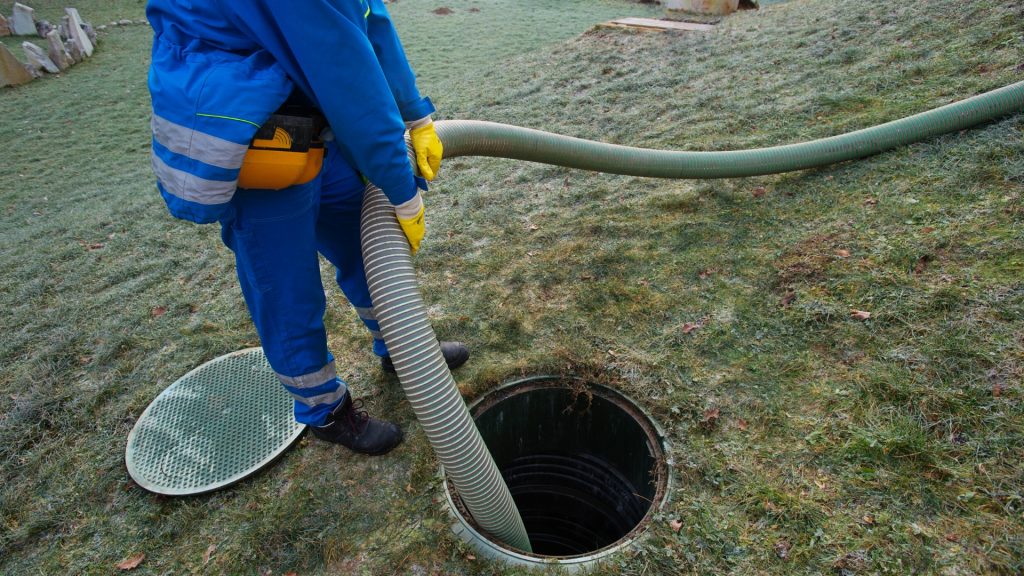 Individual in a blue protective suit pumping a septic.