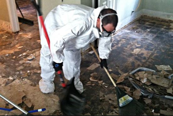 Man in protective white suit sweeps up debris off the floor from a flood