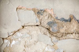 A cracked concrete wall with paint chipping off exposing raw concrete